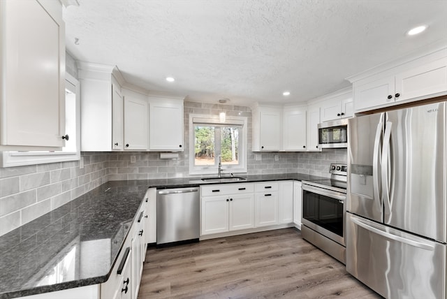 kitchen featuring tasteful backsplash, light wood-type flooring, stainless steel appliances, white cabinetry, and a sink