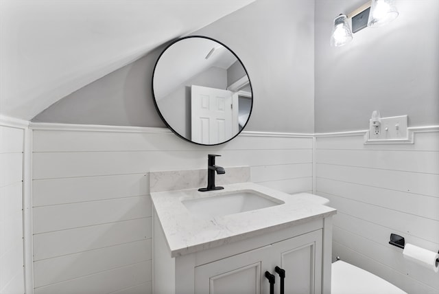 half bathroom with vanity, toilet, and wainscoting