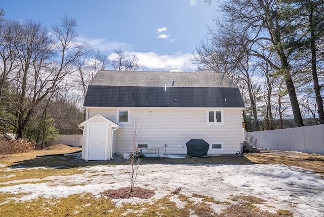 rear view of property with a storage unit, roof with shingles, an outdoor structure, and fence