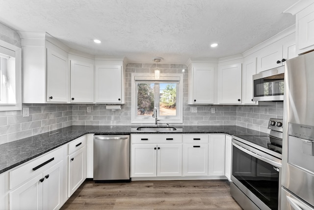 kitchen with light wood-style flooring, a sink, dark stone counters, appliances with stainless steel finishes, and white cabinets