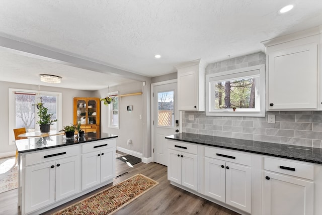 kitchen with backsplash, wood finished floors, dark stone counters, white cabinets, and baseboards