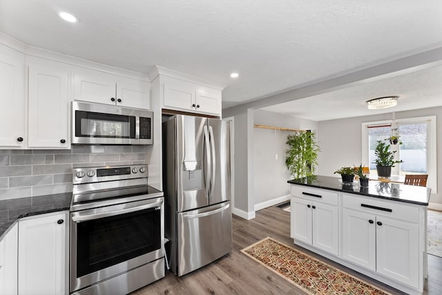 kitchen featuring wood finished floors, recessed lighting, appliances with stainless steel finishes, white cabinetry, and backsplash