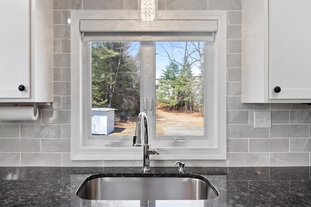 kitchen with decorative backsplash, dark stone countertops, white cabinets, and a sink