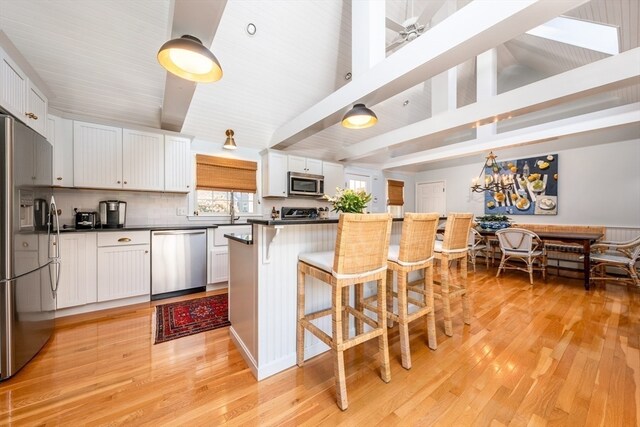 kitchen with appliances with stainless steel finishes, a breakfast bar, tasteful backsplash, white cabinets, and light wood-type flooring