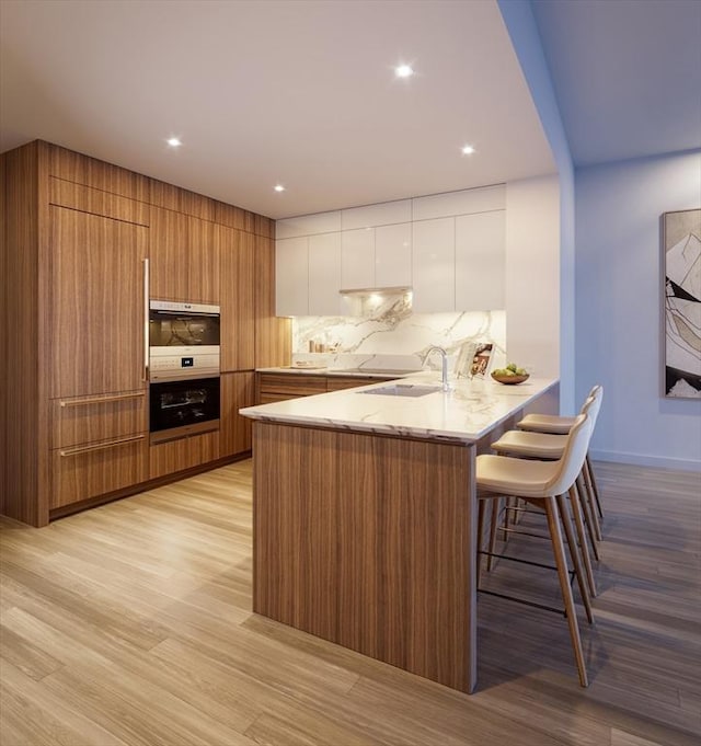 kitchen with sink, light wood-type flooring, a kitchen breakfast bar, kitchen peninsula, and white cabinets