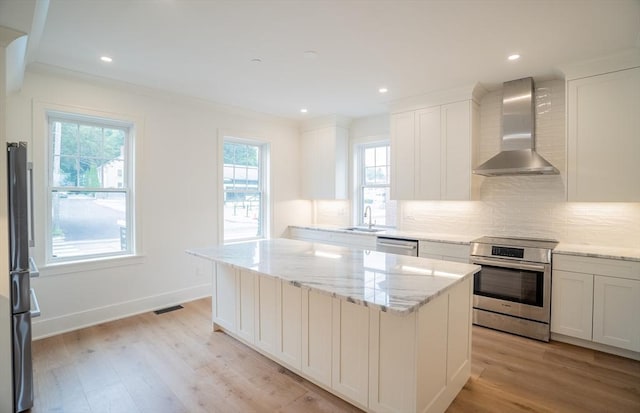 182 Merrimac St Unit 1, Newburyport, MA 01950 - kitchen with wall chimney exhaust hood, appliances with stainless steel finishes, decorative backsplash, light wood-style flooring, and white cabinetry