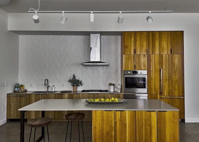 kitchen featuring brown cabinets, a sink, wall chimney exhaust hood, backsplash, and modern cabinets