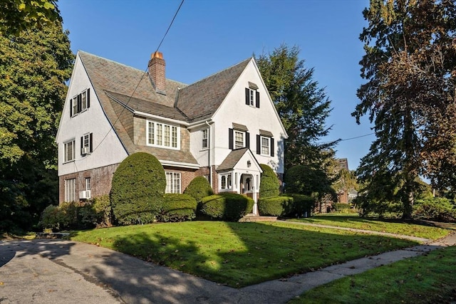 view of front of house with brick siding, a chimney, stucco siding, a shingled roof, and a front lawn