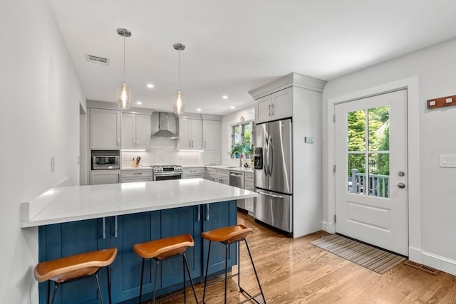 57 Glenham St, Boston, MA 02132 - kitchen with wall chimney range hood, stainless steel appliances, a peninsula, light wood-type flooring, and a kitchen breakfast bar