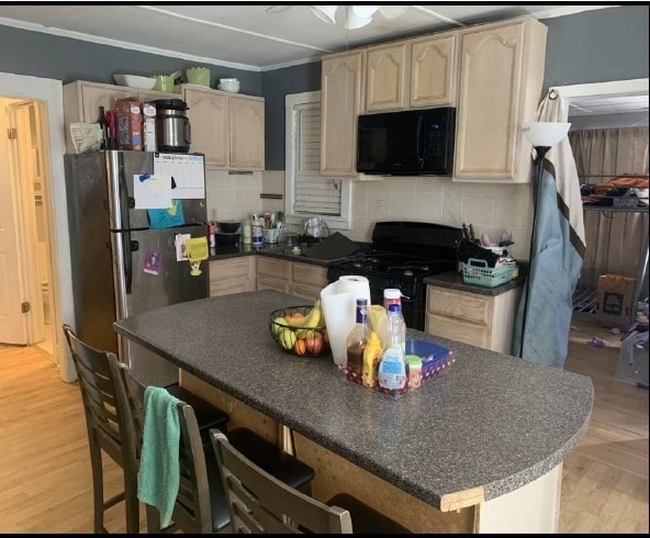 kitchen with black appliances, light wood-type flooring, decorative backsplash, a kitchen breakfast bar, and ornamental molding