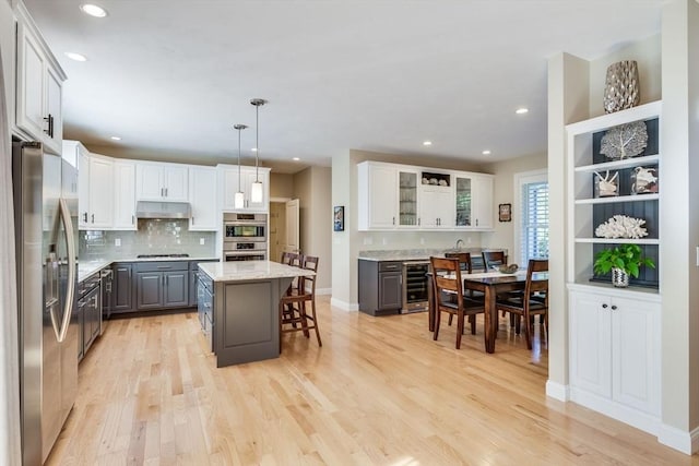 kitchen featuring gray cabinetry, beverage cooler, under cabinet range hood, a breakfast bar, and stainless steel appliances