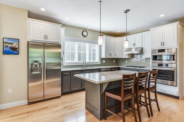 kitchen featuring light wood-type flooring, white cabinets, under cabinet range hood, appliances with stainless steel finishes, and tasteful backsplash