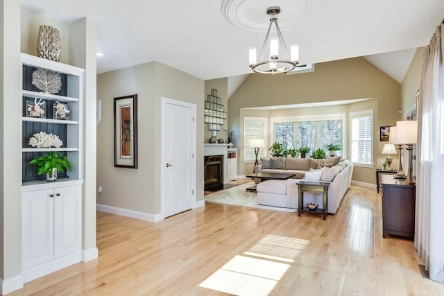 living area featuring light wood finished floors, built in features, vaulted ceiling, an inviting chandelier, and a glass covered fireplace