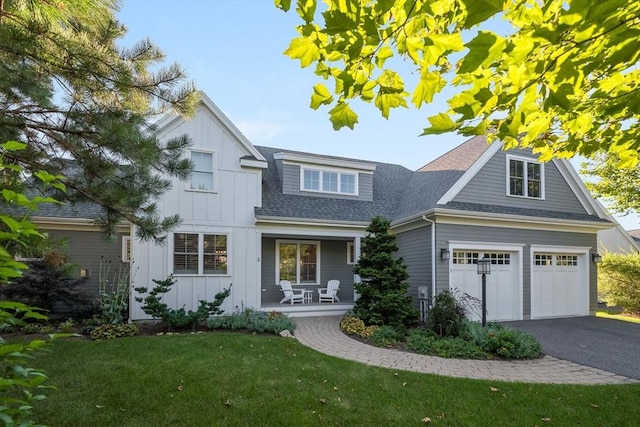 view of front facade with a front yard, roof with shingles, a porch, aphalt driveway, and board and batten siding