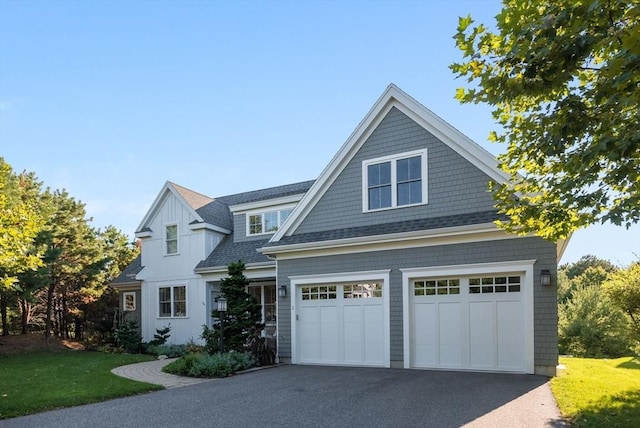 shingle-style home featuring board and batten siding, a shingled roof, a front lawn, a garage, and driveway