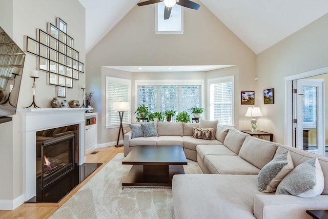 living room with a ceiling fan, baseboards, high vaulted ceiling, a high end fireplace, and light wood-style floors