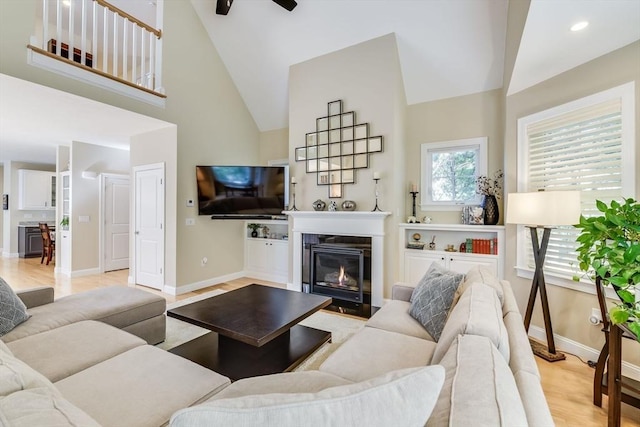 living room with baseboards, light wood-style floors, a glass covered fireplace, and high vaulted ceiling