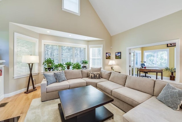 living room featuring a healthy amount of sunlight, high vaulted ceiling, light wood-type flooring, and baseboards