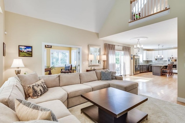 living room with an inviting chandelier, light wood-type flooring, and high vaulted ceiling