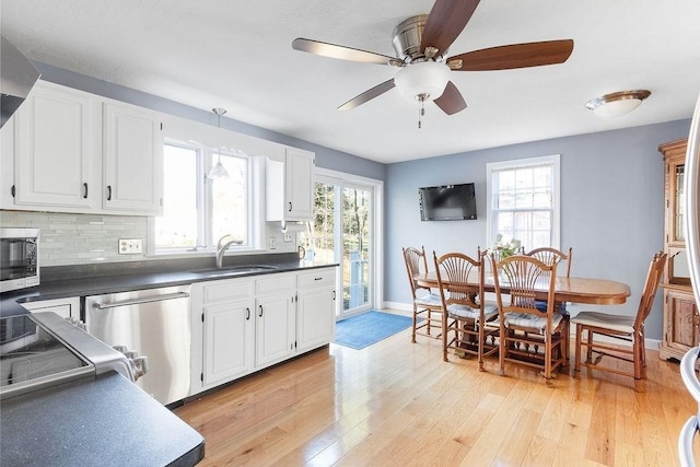 kitchen featuring decorative backsplash, dark countertops, appliances with stainless steel finishes, light wood-type flooring, and a sink