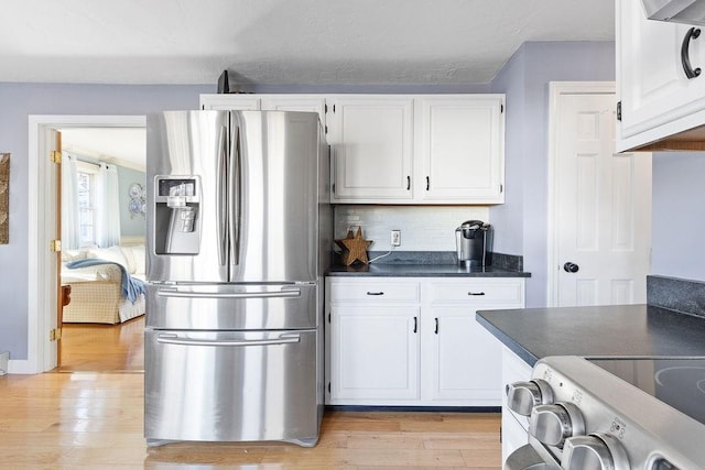 kitchen featuring dark countertops, light wood-type flooring, stainless steel fridge, and white cabinetry