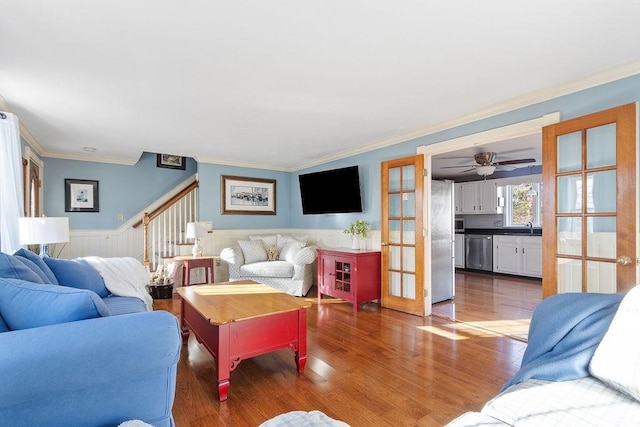 living area with a wainscoted wall, wood finished floors, stairs, french doors, and ornamental molding