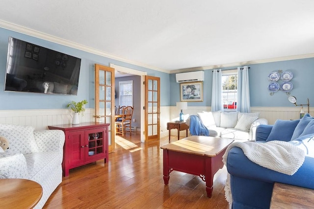 living room with wood finished floors, ornamental molding, french doors, a wall mounted AC, and wainscoting