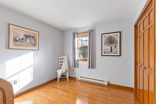 living area with a baseboard heating unit, light wood-type flooring, and baseboards