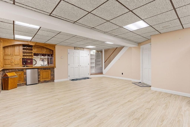 finished basement with a paneled ceiling, stairway, light wood-style floors, baseboards, and fridge