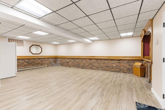 basement with a drop ceiling, brick wall, wood finished floors, freestanding refrigerator, and baseboard heating