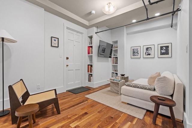 sitting room with wood finished floors, built in shelves, and recessed lighting