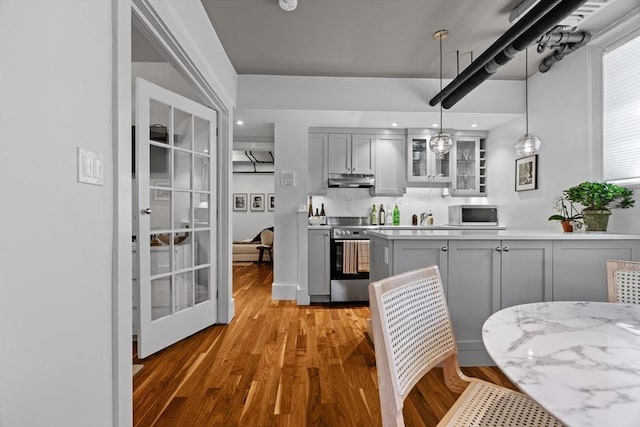 kitchen featuring stainless steel electric range oven, gray cabinets, light wood-style floors, under cabinet range hood, and glass insert cabinets