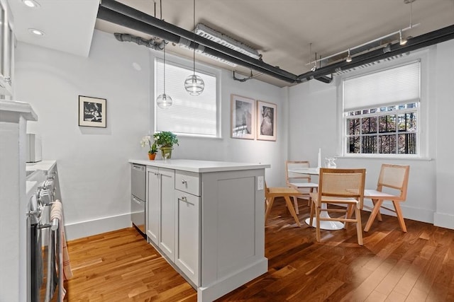 kitchen featuring a peninsula, light wood-type flooring, baseboards, light countertops, and decorative light fixtures