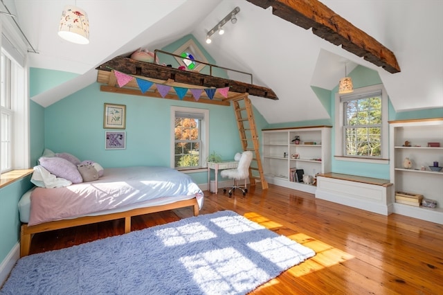 bedroom with multiple windows, lofted ceiling with beams, track lighting, and wood-type flooring