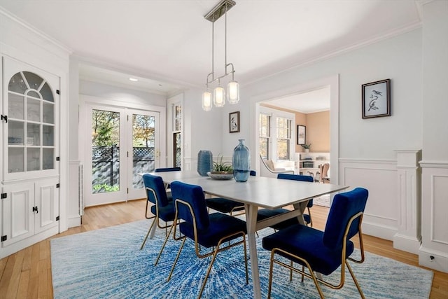 dining room featuring ornamental molding, light wood finished floors, a wainscoted wall, and a healthy amount of sunlight