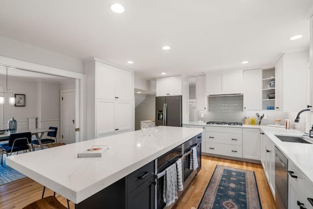 kitchen with a center island, white cabinetry, a sink, backsplash, and stainless steel appliances