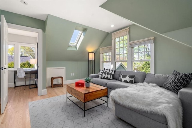 living room featuring vaulted ceiling with skylight, baseboards, and wood finished floors