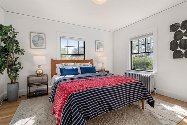 bedroom featuring baseboards, radiator heating unit, and light wood-type flooring