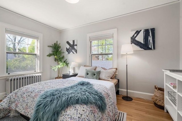 bedroom featuring baseboards, multiple windows, radiator, and light wood-style floors