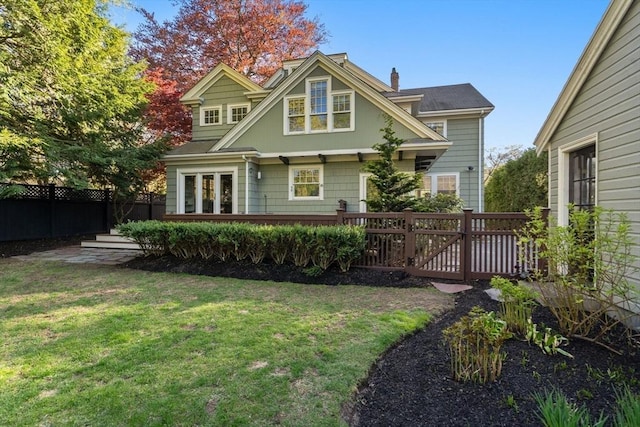 rear view of house featuring fence, a wooden deck, a chimney, and a yard