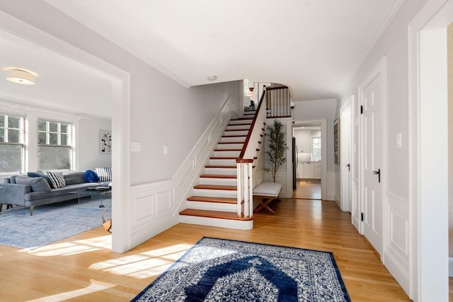 stairs featuring ornamental molding, a decorative wall, wood finished floors, and a healthy amount of sunlight