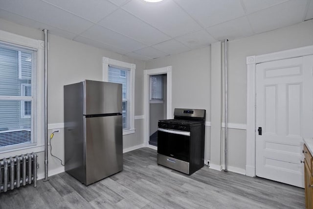 kitchen featuring radiator heating unit, light hardwood / wood-style floors, appliances with stainless steel finishes, and a drop ceiling