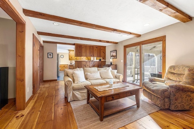 living area featuring light wood-type flooring, a textured ceiling, baseboards, and beam ceiling