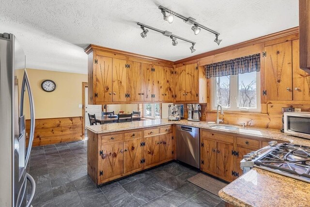 kitchen featuring a wainscoted wall, brown cabinets, appliances with stainless steel finishes, a textured ceiling, and a peninsula