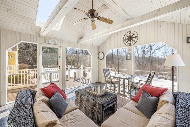 living room featuring ceiling fan, wood walls, and lofted ceiling with skylight