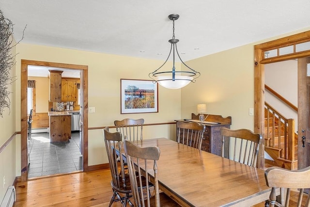 dining space featuring a baseboard heating unit, stairs, and light wood-style floors