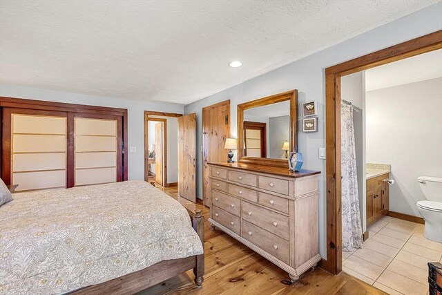 bedroom with light wood-style flooring, a textured ceiling, baseboards, and ensuite bathroom