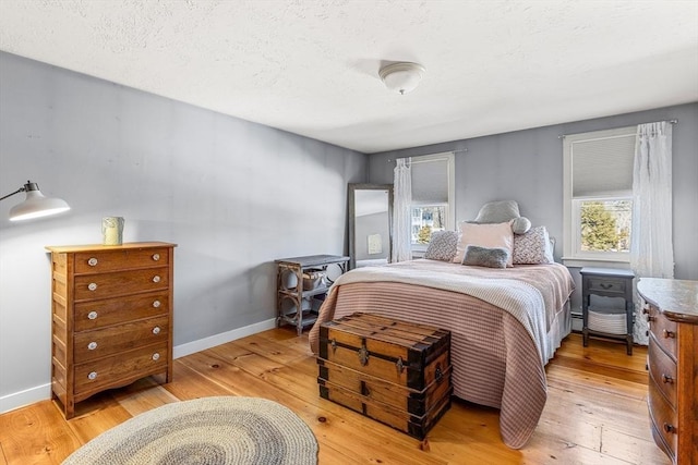 bedroom featuring baseboards, a textured ceiling, and light wood finished floors