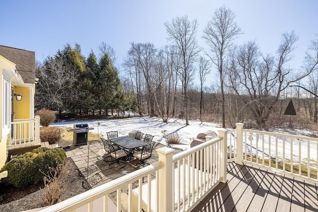 snow covered deck with outdoor dining space, a patio, and area for grilling