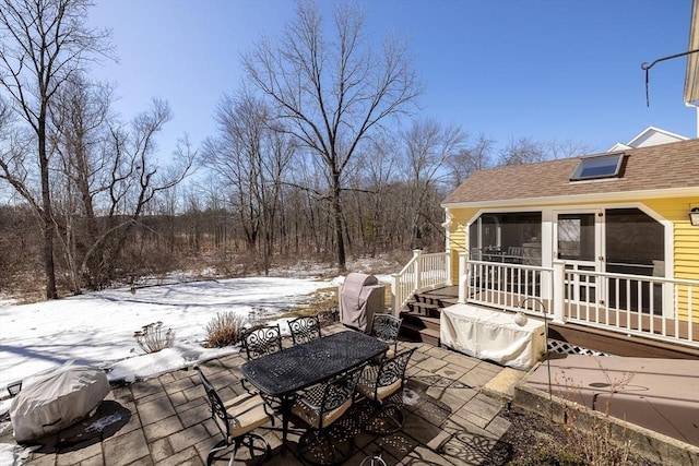 snow covered patio with outdoor dining area, a wooden deck, and a sunroom